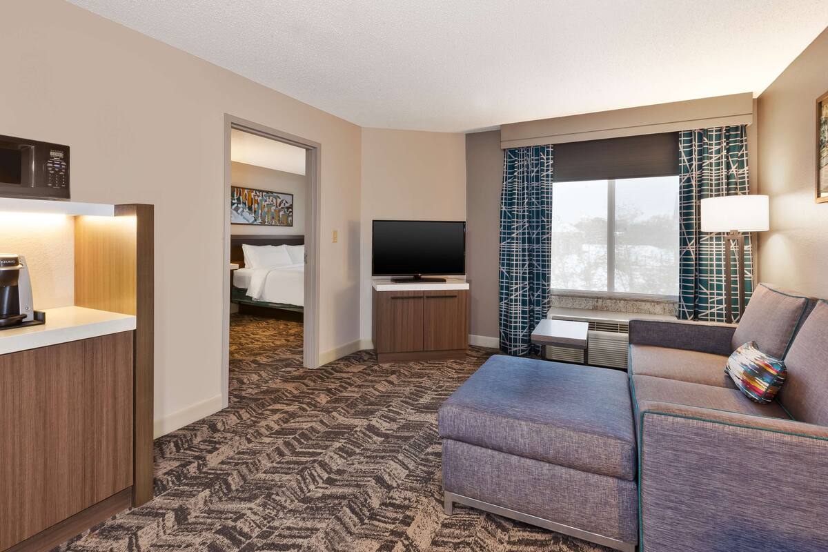 A hotel room with a sofa, a television, a coffee maker, and a painting on the wall.