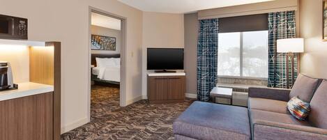 A hotel room with a sofa, a television, a coffee maker, and a painting on the wall.