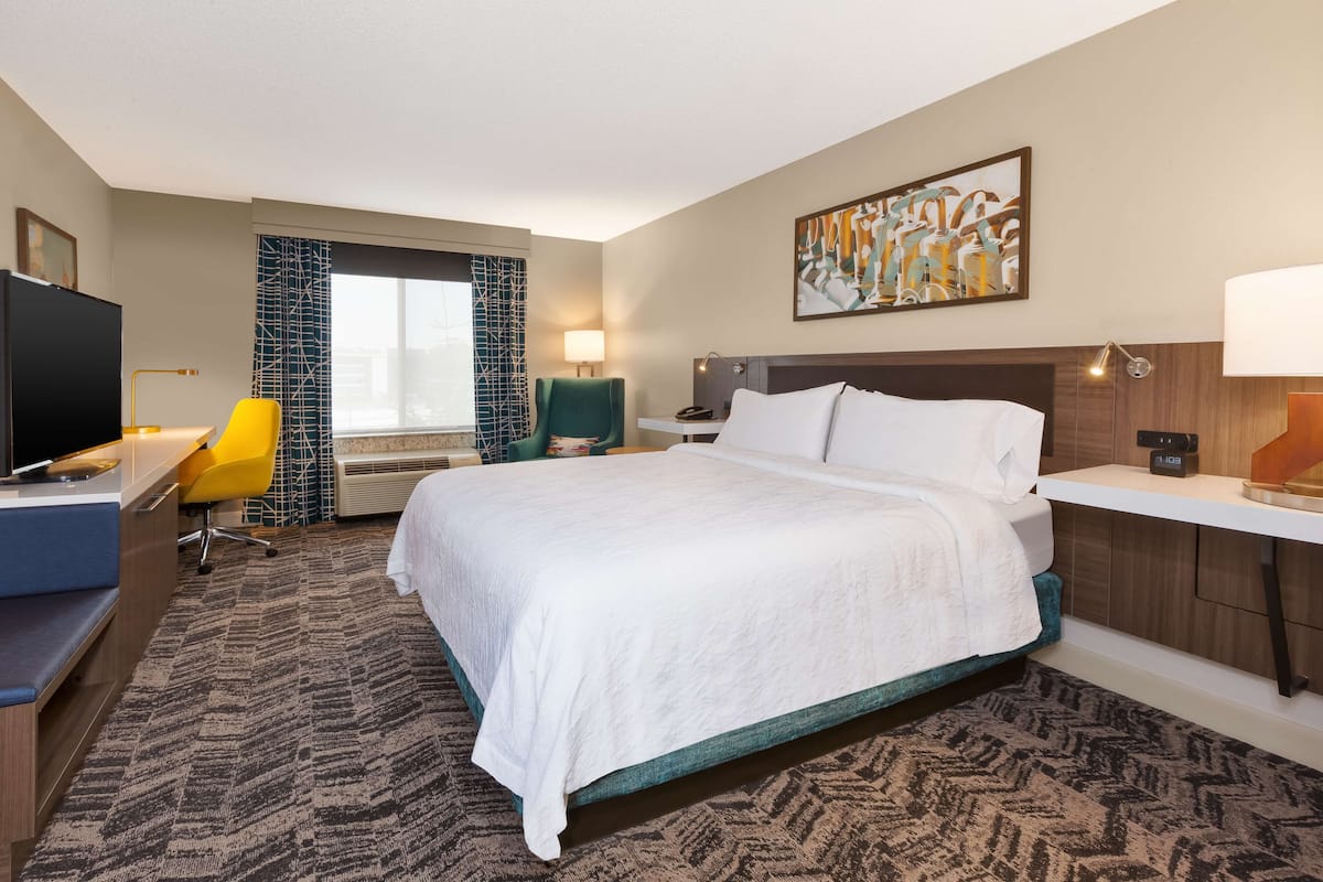 A hotel room with a large bed, a desk with a chair, a TV, and a window with curtains.