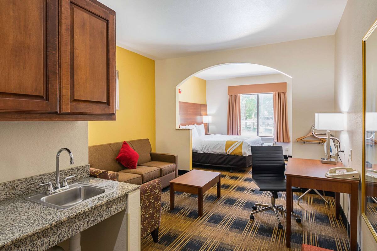 A hotel room with a kitchenette, a sofa, a desk, and a bed.