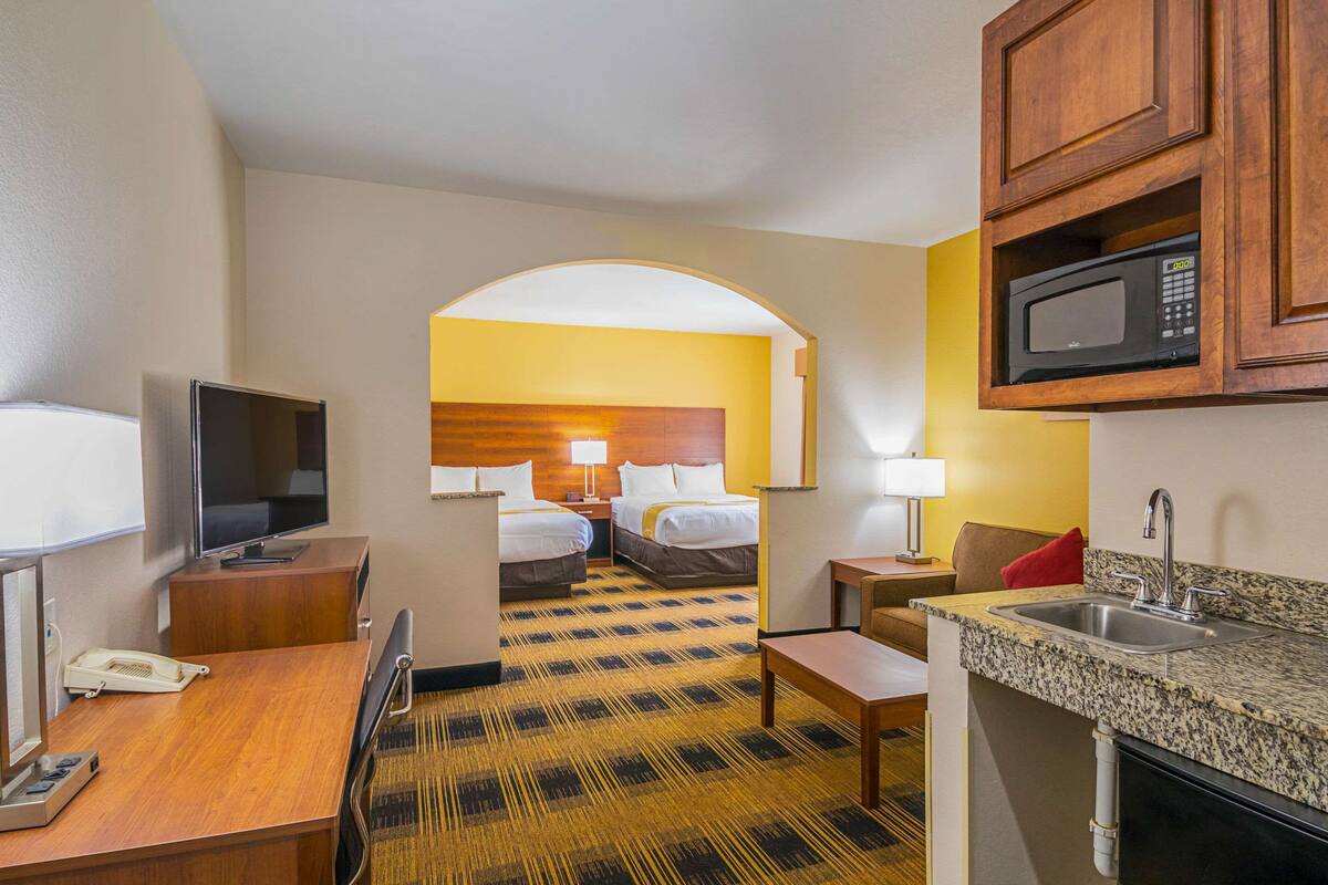 A hotel room with a TV, desk, two beds, a microwave, and a sink.
