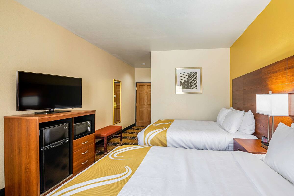 A hotel room with two beds, a flat-screen TV, a minibar, and a wooden headboard.