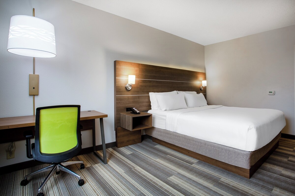 A hotel room with a bed, a desk, a chair, a lamp, and a nightstand.