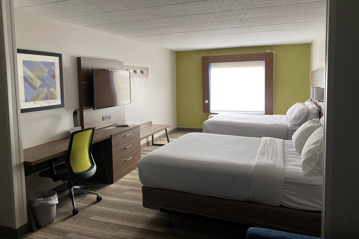 A hotel room with a bed, a desk with a chair, a television, and a window.