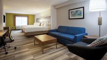 A hotel room with a bed, a blue sofa, a small table, a chair, and a lamp.