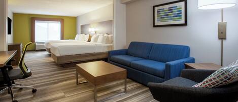 A hotel room with a bed, a blue sofa, a small table, a chair, and a lamp.