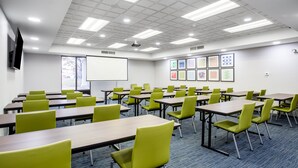A conference room with multiple tables and chairs, a projector screen, and framed artwork on the walls. - Holiday Inn Express & Suites Fort Wayne by IHG (Fort Wayne)