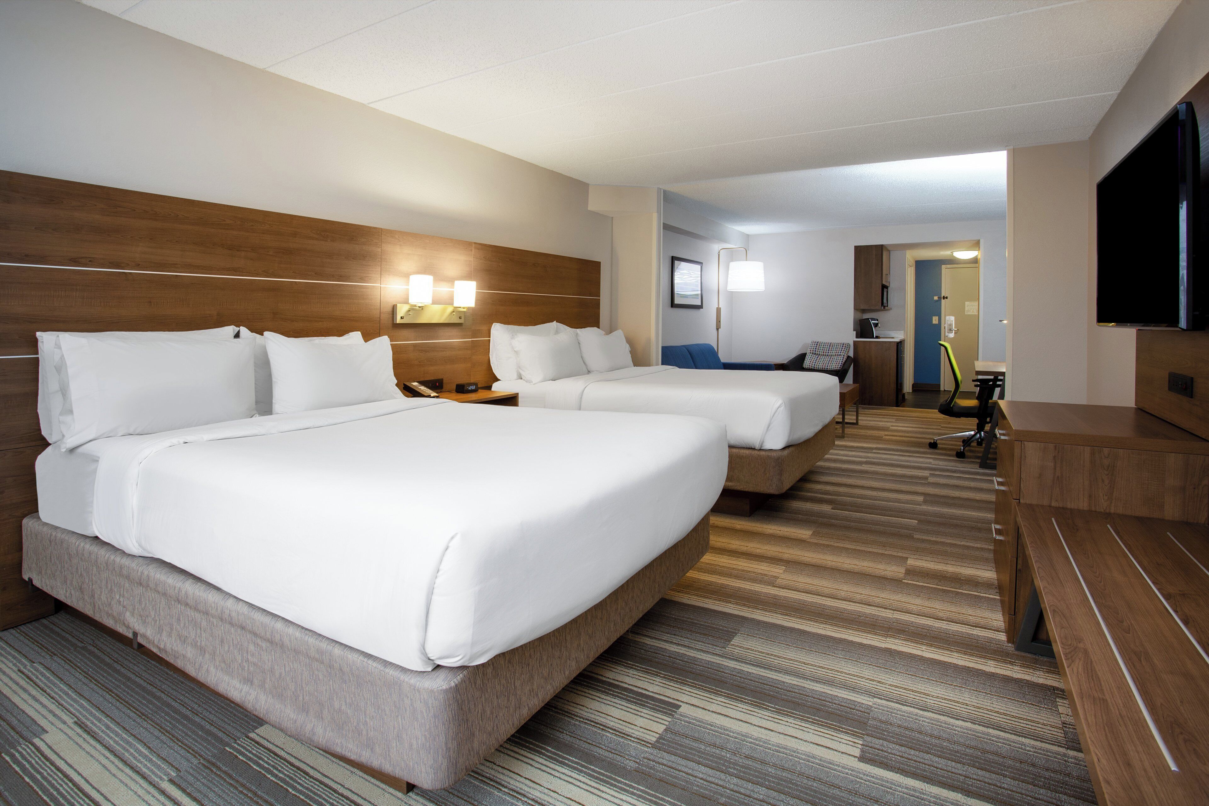 Ein Hotelzimmer mit zwei Betten, einem Schreibtisch, einem Stuhl, einem Fernseher und einem sichtbaren Badezimmer im Hintergrund.