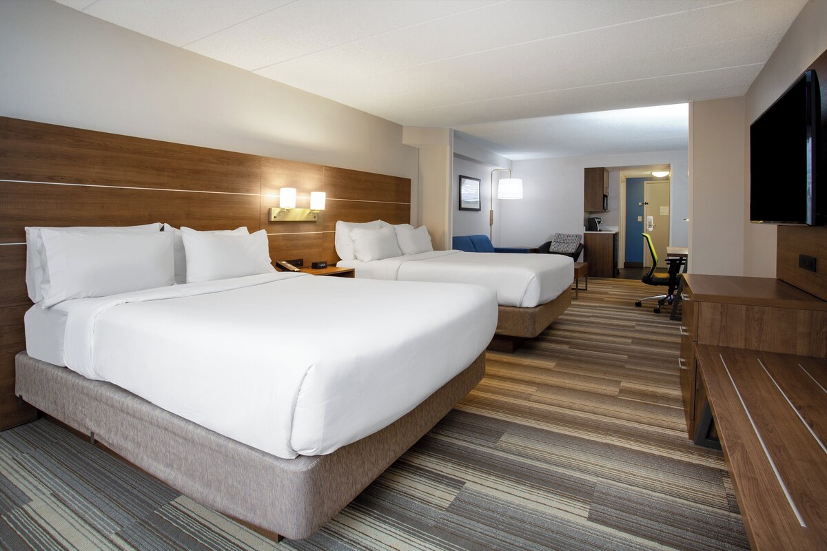 A hotel room with two beds, a desk, a chair, a TV, and a bathroom visible in the background.