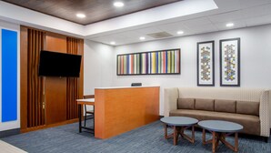 A reception area with a wooden desk, two round tables, a sofa, and a TV on the wall. - Holiday Inn Express & Suites Fort Wayne by IHG (Fort Wayne)