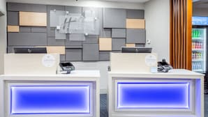 A reception area with two reception desks, each equipped with a digital kiosk and a phone. The walls are decorated with geometric patterns and a sign for 'Holiday Inn Express & Suites'. - Holiday Inn Express & Suites Fort Wayne by IHG (Fort Wayne)