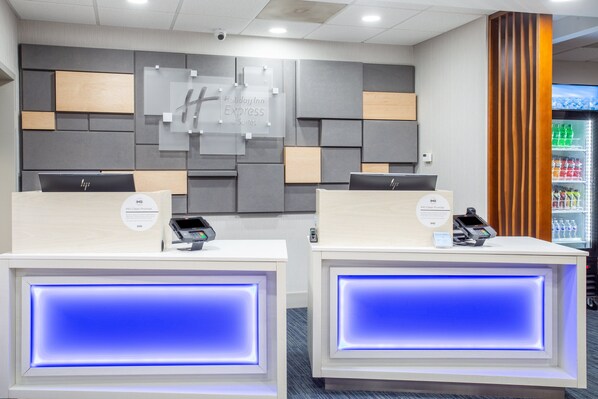A reception area with two reception desks, each equipped with a digital kiosk and a phone. The walls are decorated with geometric patterns and a sign for 'Holiday Inn Express & Suites'. - Holiday Inn Express & Suites Fort Wayne by IHG (Fort Wayne)