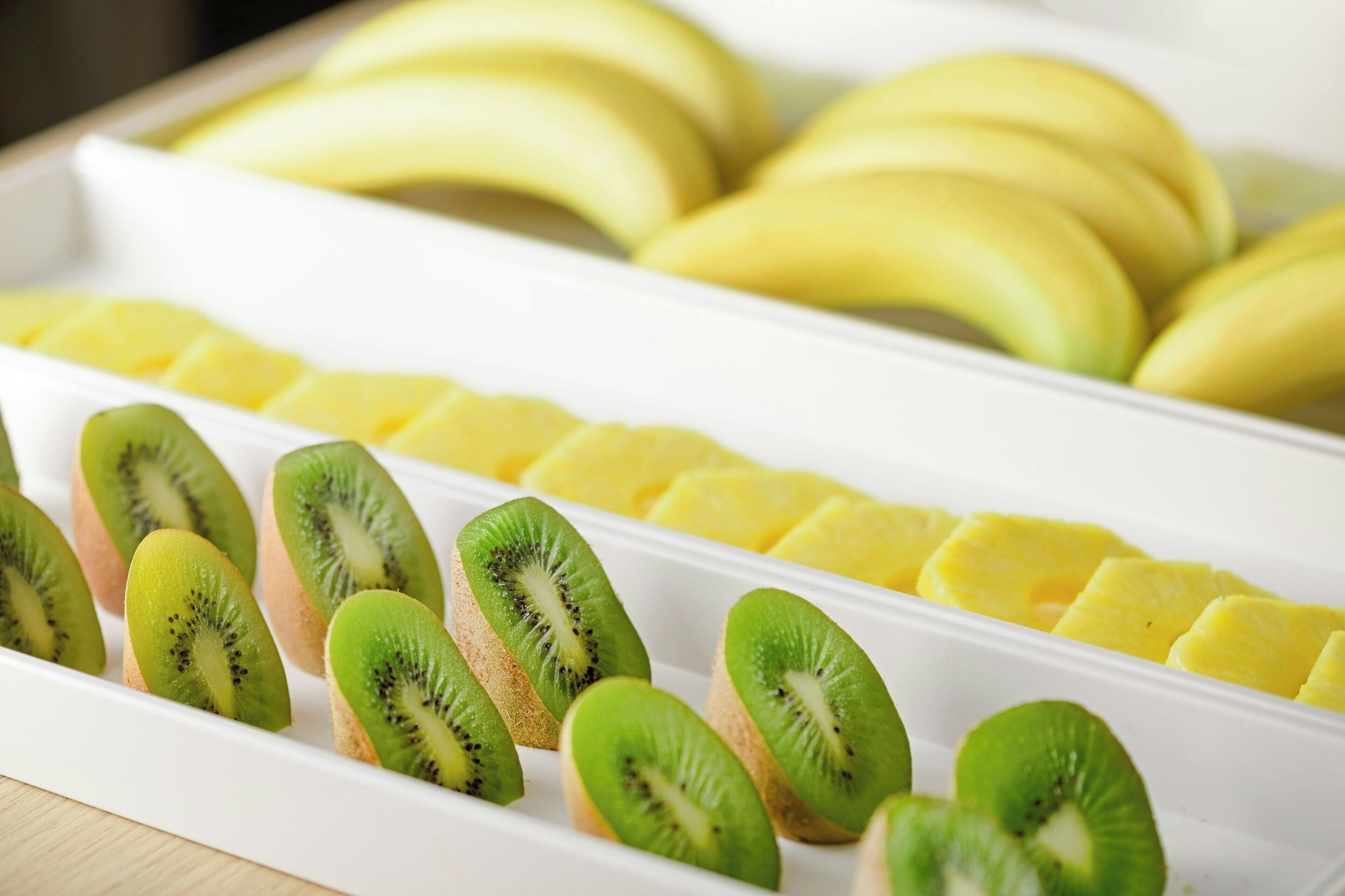 Un plateau de fruits coupés en tranches, notamment des bananes et des kiwis.