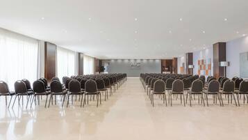 A large, well-lit conference room with rows of chairs facing a stage.