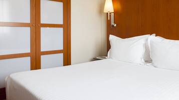 A hotel room with a large bed, wooden wardrobe, and a wall-mounted lamp.