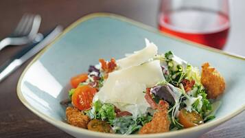 A bowl of salad with croutons, cheese, and tomatoes on a table.