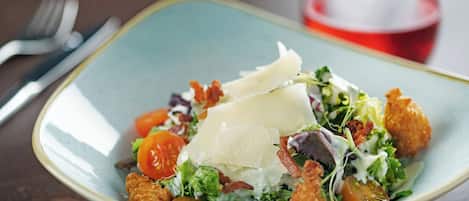 A bowl of salad with croutons, cheese, and tomatoes on a table.