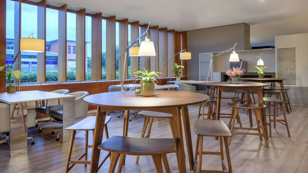 A modern dining area with round tables, wooden chairs, and pendant lighting. - AC Hotel Sevilla Fórum by Marriott (Seville)