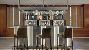 A bar area with a black countertop, two bar stools, and a shelf with various bottles and glasses. - AC Hotel Sevilla Fórum by Marriott (Seville)