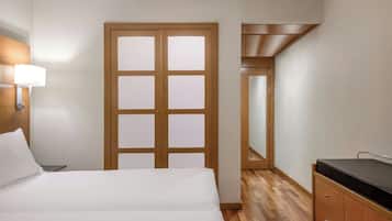 Habitación de hotel con una cama, una mesita de noche, una lámpara, un armario de madera y una puerta con paneles de vidrio esmerilado.