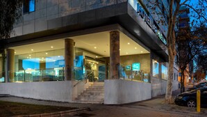 Una entrada de hotel moderna con puertas de vidrio, una escalera y un letrero de estacionamiento visible.
