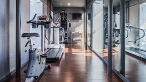 Un gimnasio moderno con máquinas de cardio, una cinta de correr y un espejo grande.
