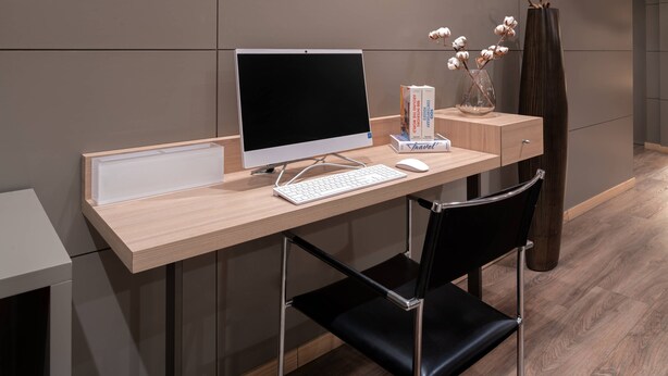 A modern office desk with a computer, keyboard, and mouse, a black chair, and a vase with cotton plants. - AC Hotel Huelva by Marriott (Huelva)