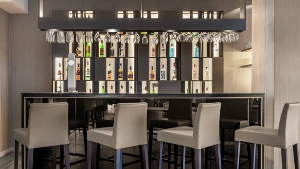 Zona de bar con una barra larga, varios taburetes y una pared llena de botellas de licor.