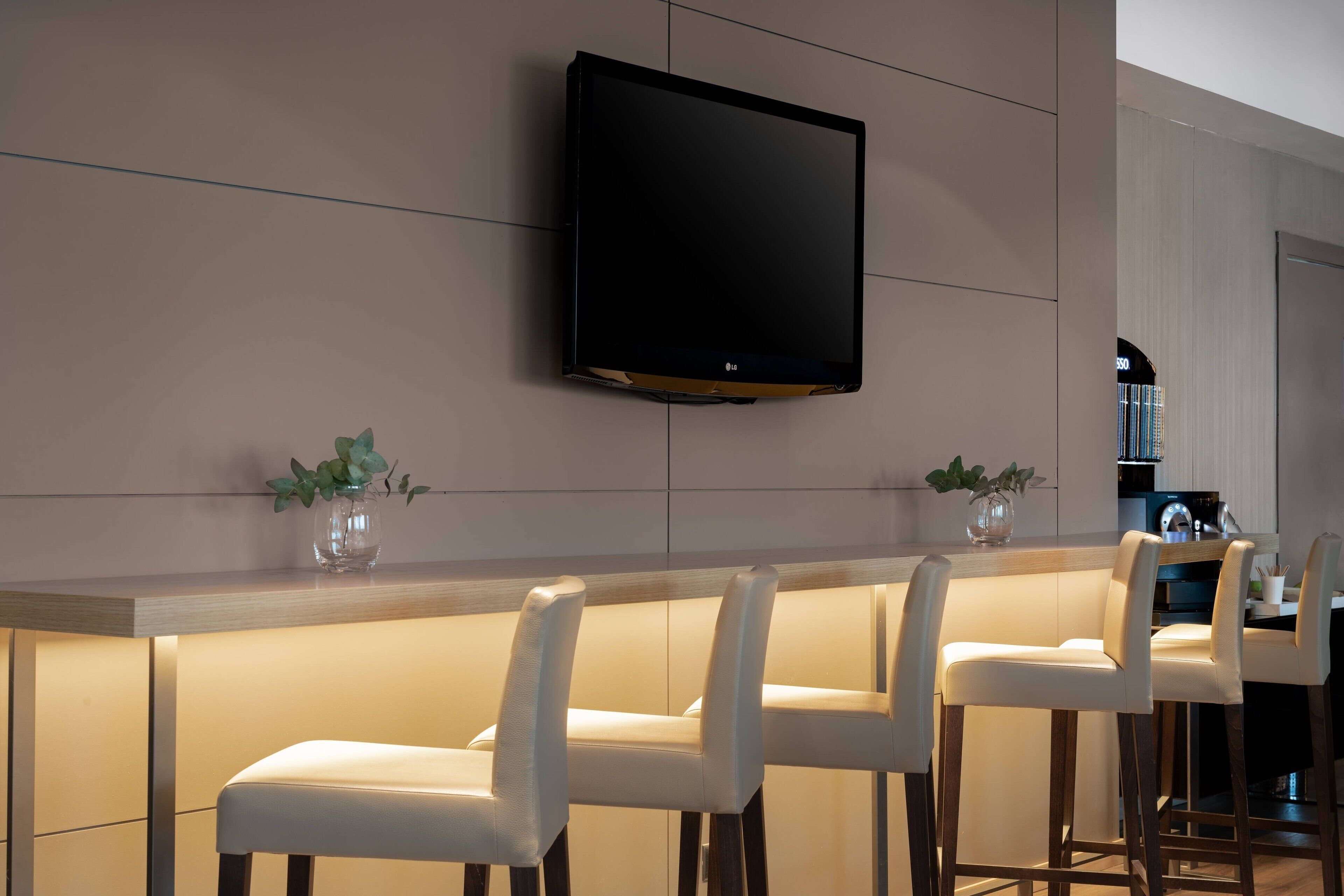 A modern kitchen with a flat-screen TV mounted on the wall, a bar area with white bar stools, and a wooden countertop.