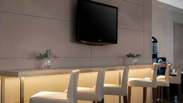 Una cocina moderna con un televisor de pantalla plana montado en la pared, una zona de bar con taburetes blancos y una encimera de madera.