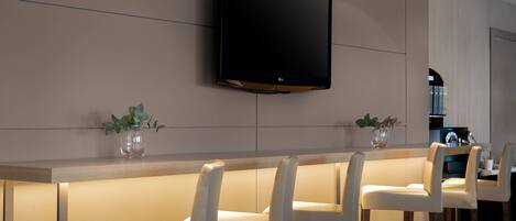 A modern kitchen with a flat-screen TV mounted on the wall, a bar area with white bar stools, and a wooden countertop.