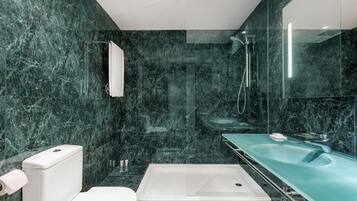 A modern bathroom with a marble wall, a white toilet, a glass-enclosed shower, and a green sink.