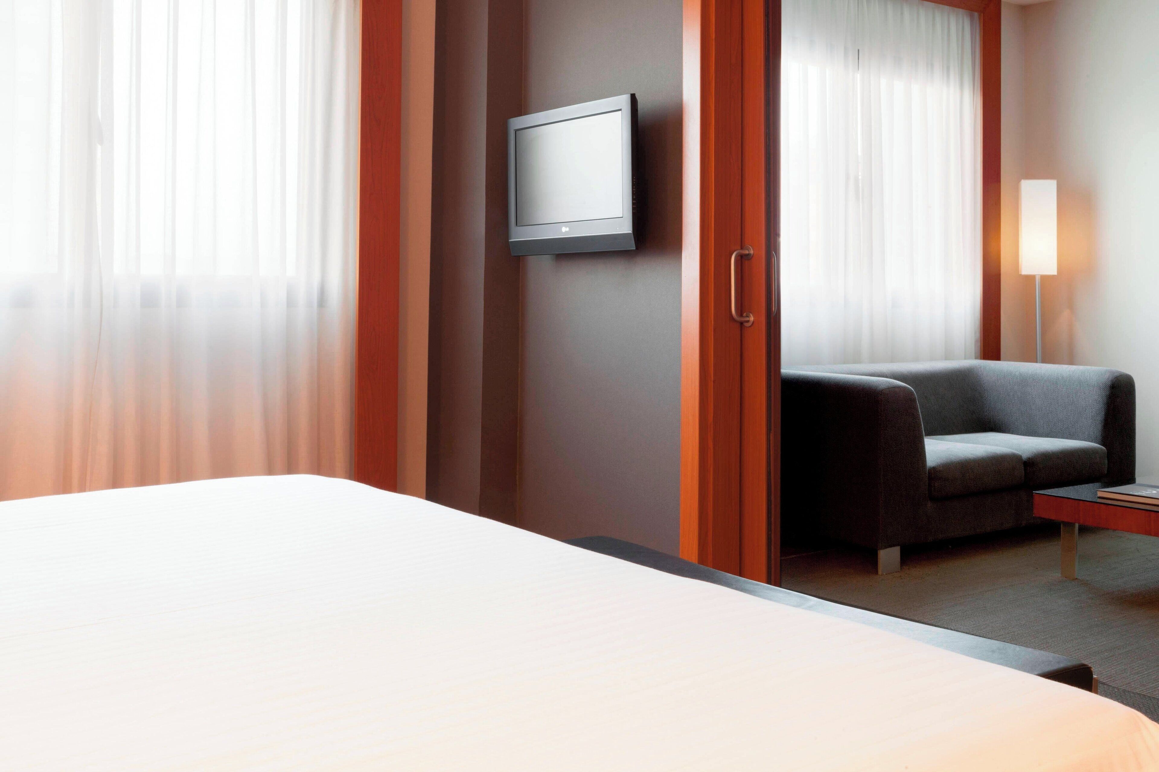 A hotel room with a bed, a TV mounted on the wall, a sofa, and a bedside table.