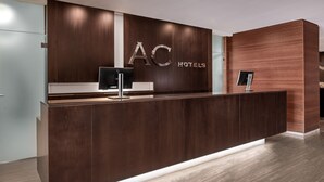 A reception desk with a dark wood finish, a flat-screen TV, and a digital display. - AC Hotel Murcia by Marriott (Murcia)