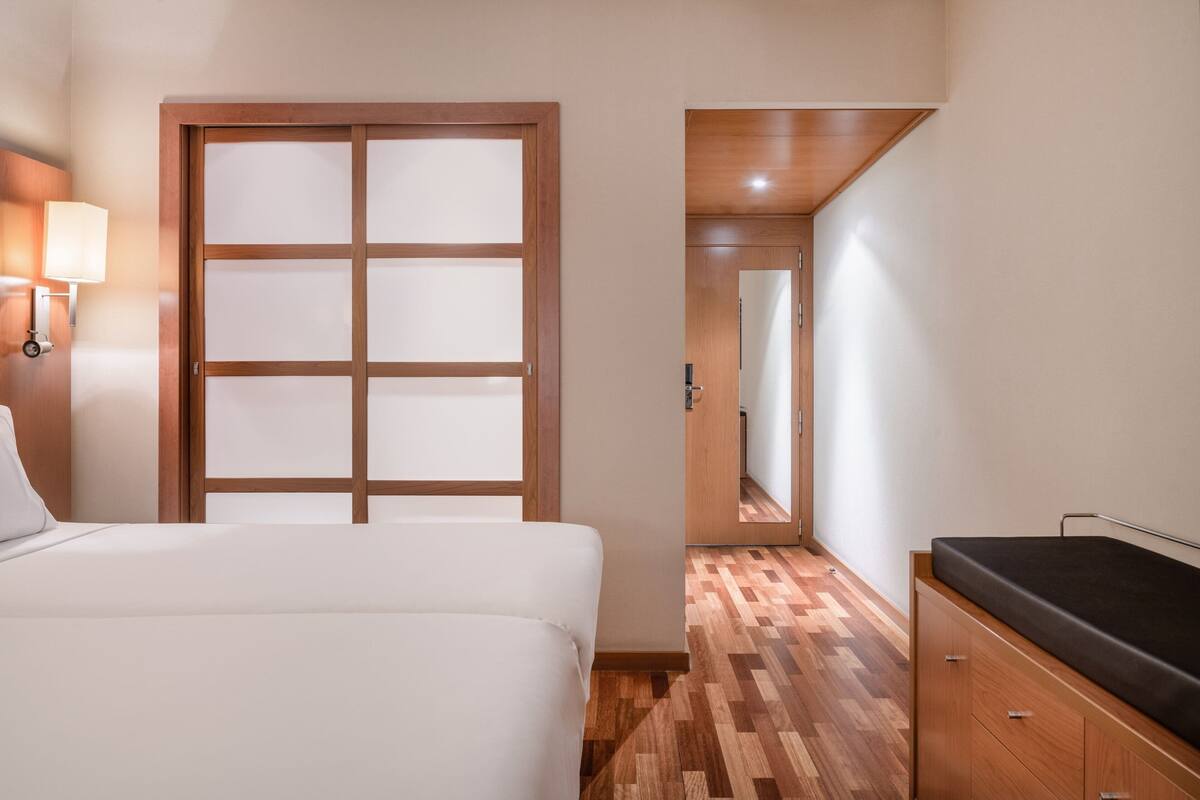 A hotel room with a bed, a wooden wardrobe, a mirror, and a door with frosted glass panels.