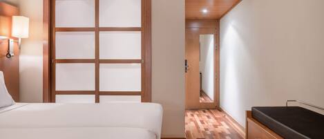 A hotel room with a bed, a wooden wardrobe, a mirror, and a door with frosted glass panels.