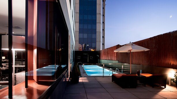 A rooftop pool area with a glass balustrade, a wooden deck, and a large umbrella. - AC Hotel Murcia by Marriott (Murcia)