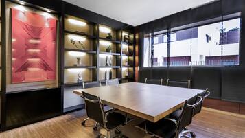 A conference room with a large table, chairs, shelves with decorative items, and a view through a window.