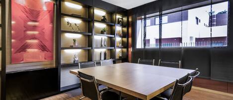 A conference room with a large table, chairs, shelves with decorative items, and a view through a window.