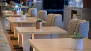 A row of wooden tables with potted plants, upholstered chairs, and a modern interior design.