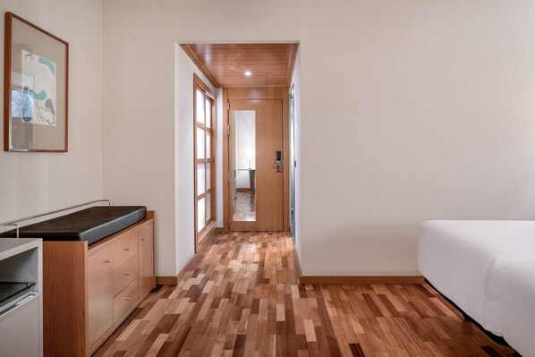 A hallway with a wooden floor, a bed on the right, and a kitchenette on the left.