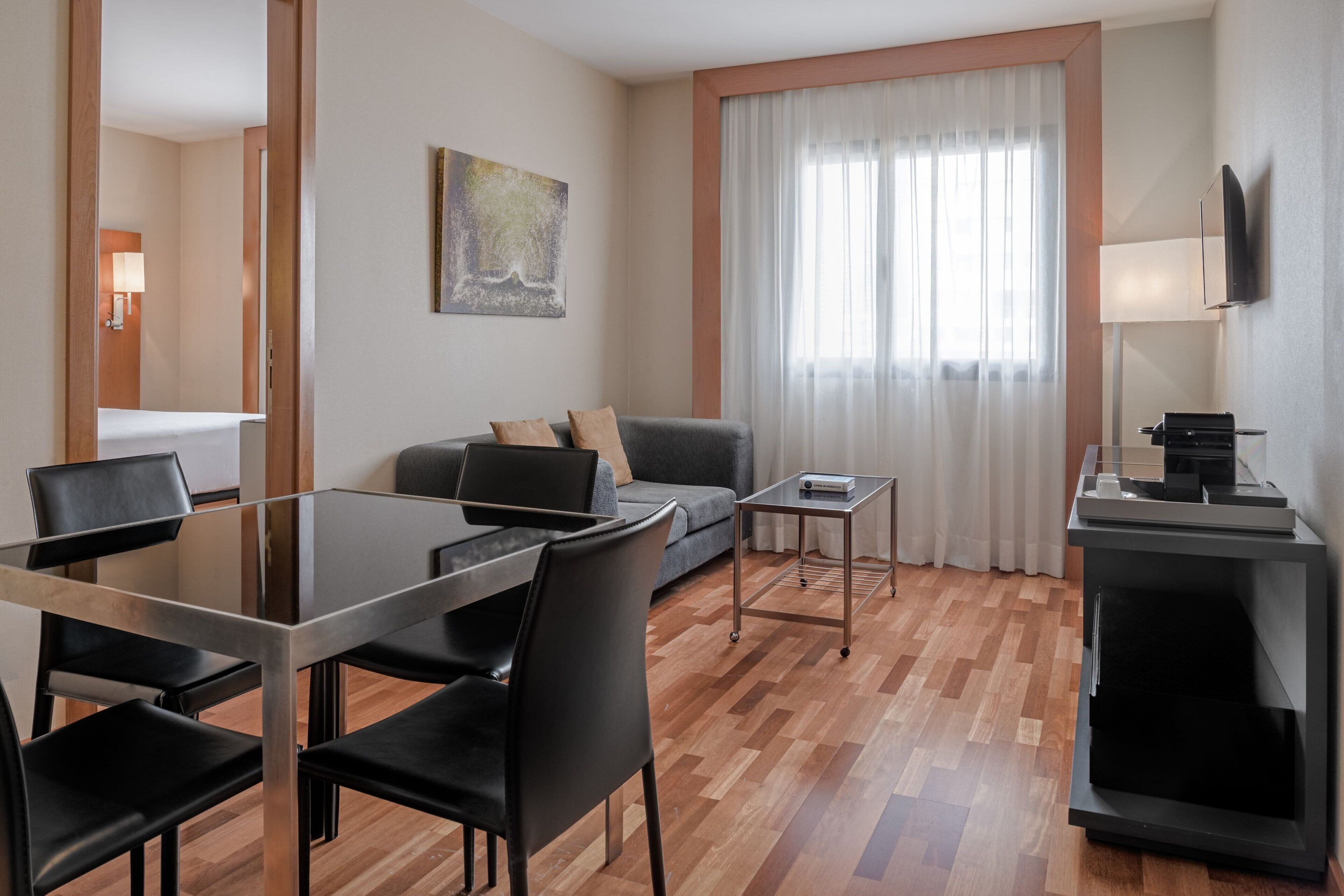 Ein modernes Hotelzimmer mit Essbereich, einer Couch, einem Fernseher und einem Fenster mit Vorhängen.