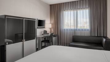 A hotel room with a bed, a desk with a chair, a TV, and a sofa.