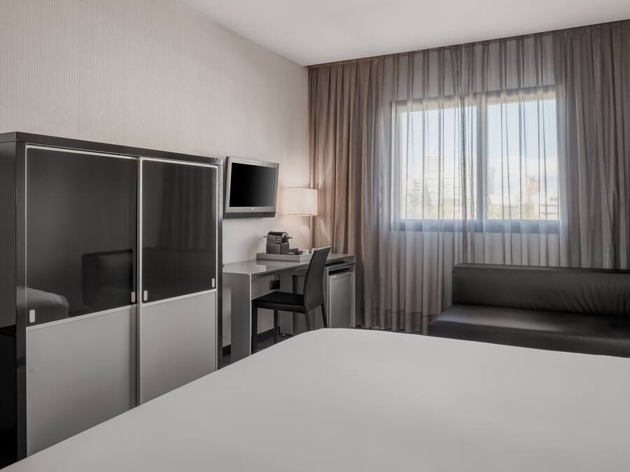 A hotel room with a bed, a desk with a chair, a TV, and a sofa.