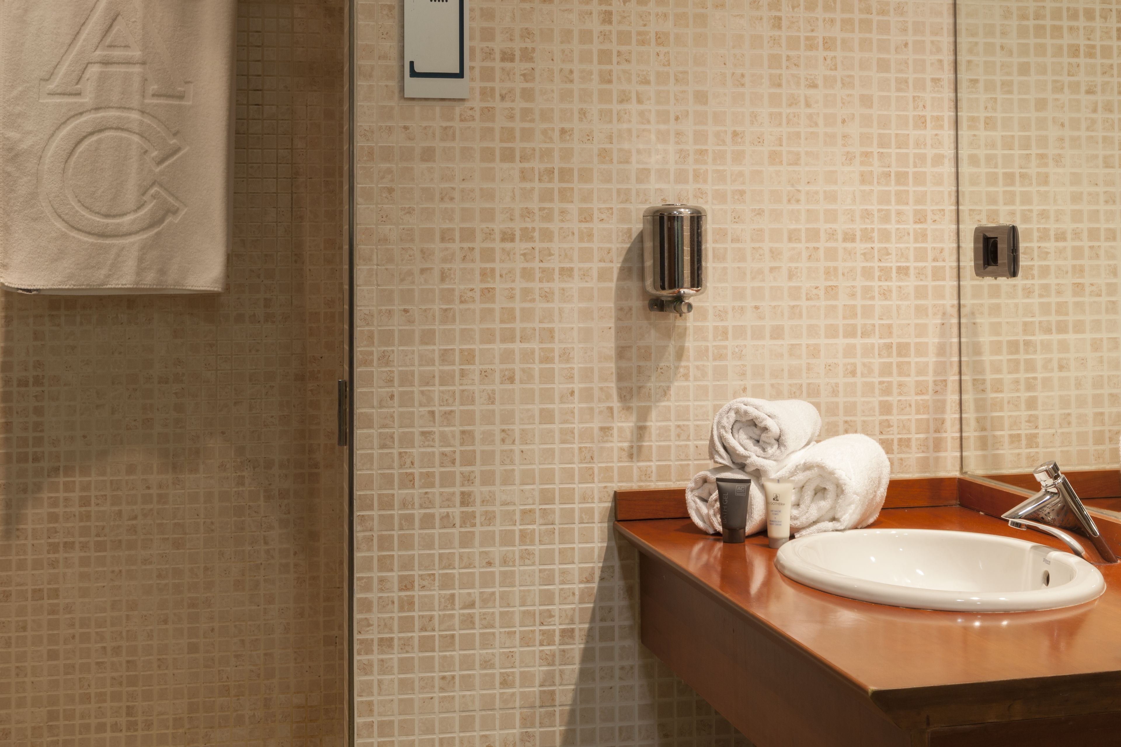 Un baño con pared de azulejos, un lavamanos, un dispensador de toallas y un espejo.