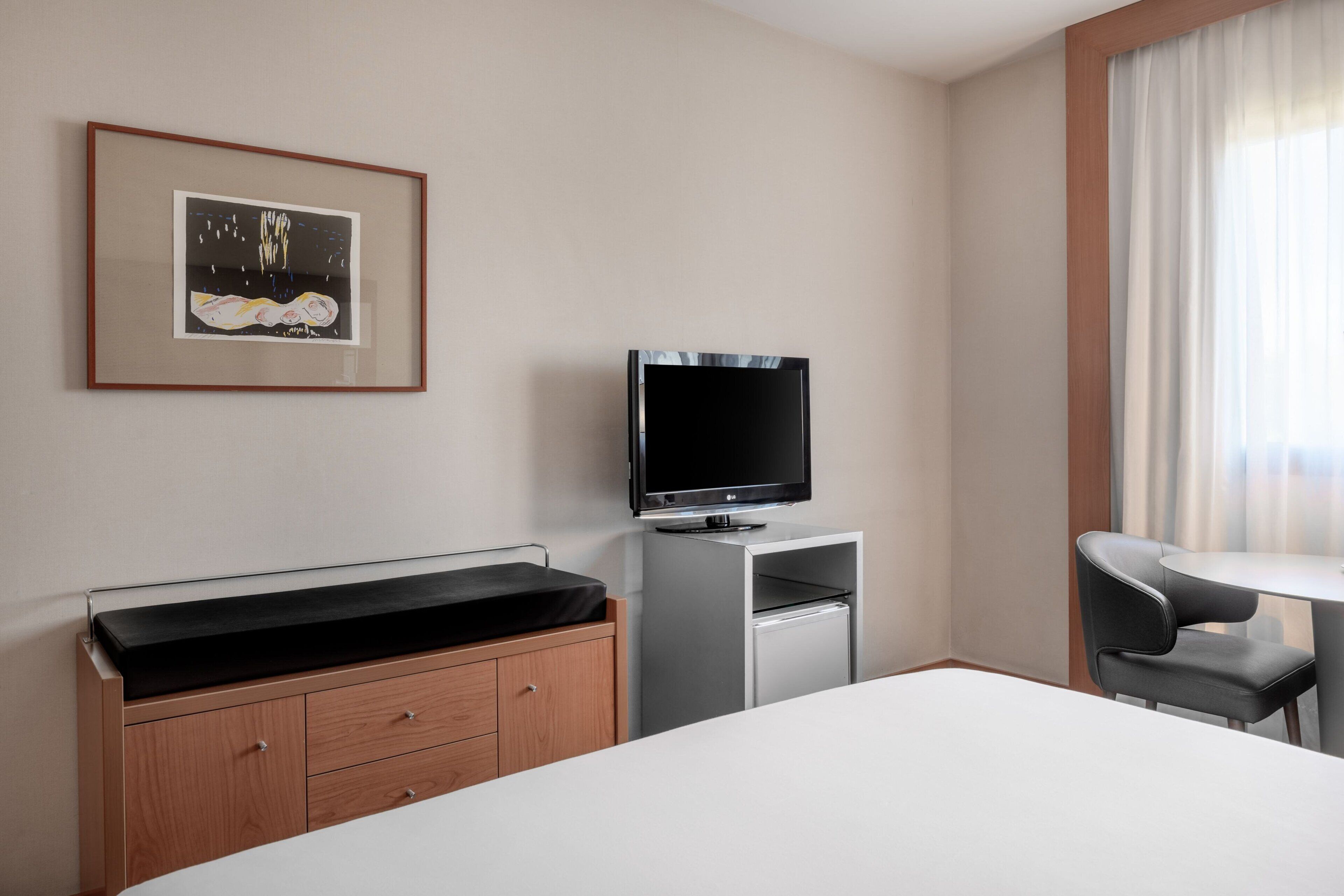 A hotel room with a bed, a desk, a television, a chair, and a framed picture on the wall.
