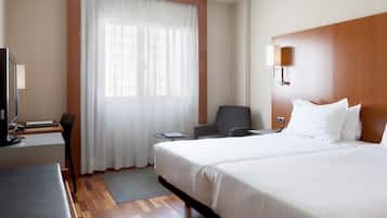 A hotel room with a bed, a desk, a chair, a TV, and a window with curtains.