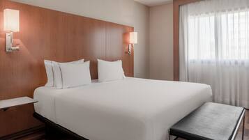 Habitación de hotel con una cama grande, dos mesitas de noche, un banco al pie de la cama y dos lámparas de pared.