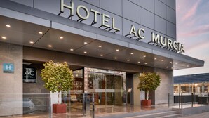 A modern hotel entrance with a glass facade, two potted trees, and a sign reading "HOTEL AC MURCIA". - AC Hotel Murcia by Marriott (Murcia)