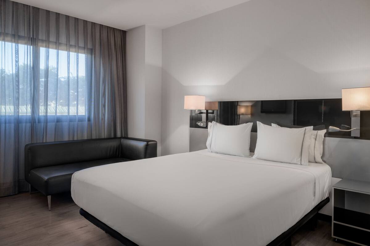 A modern hotel room with a large bed, a sofa, a TV, and a desk.